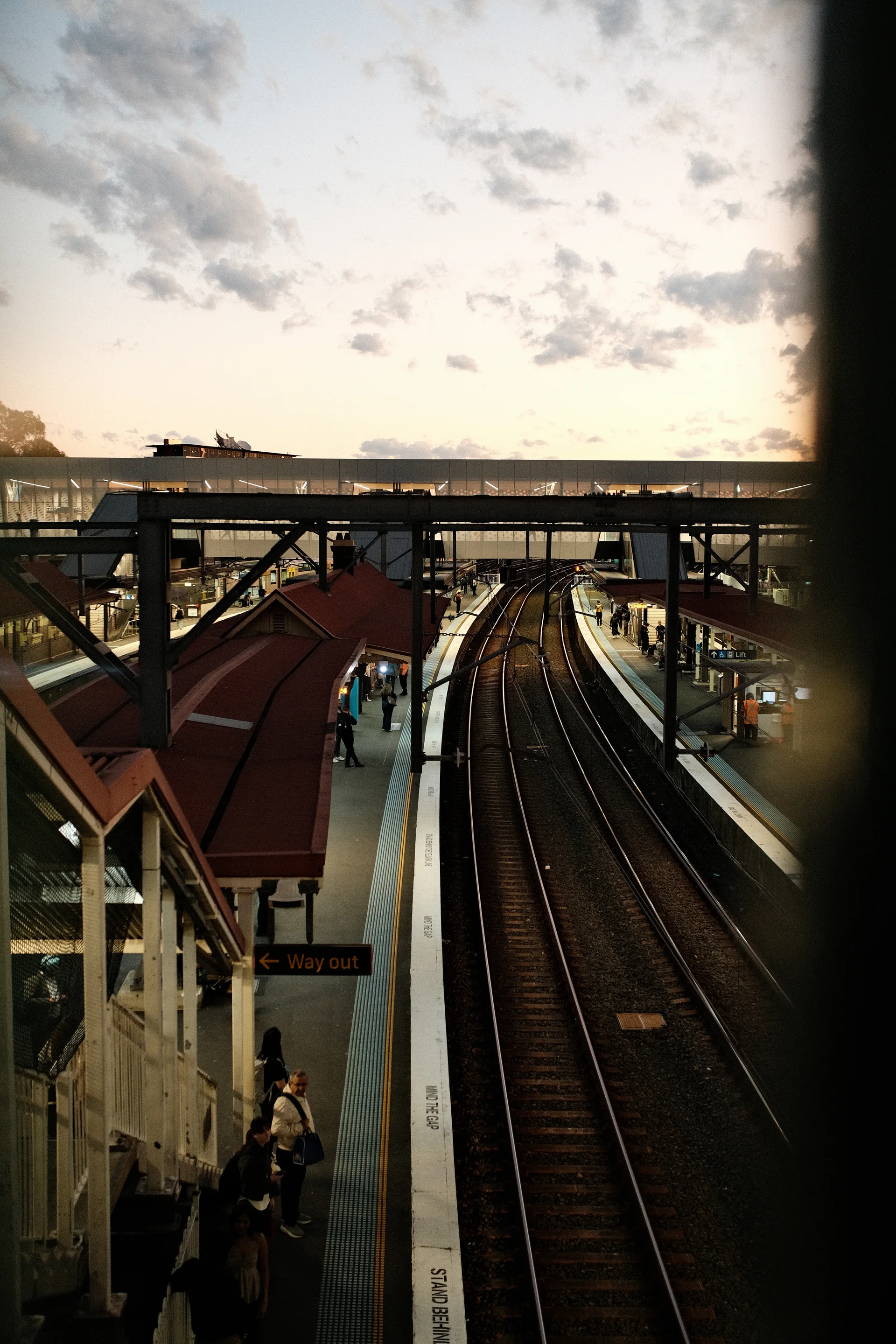 Railway platforms and converging tracks viewed from above under an evening sky.