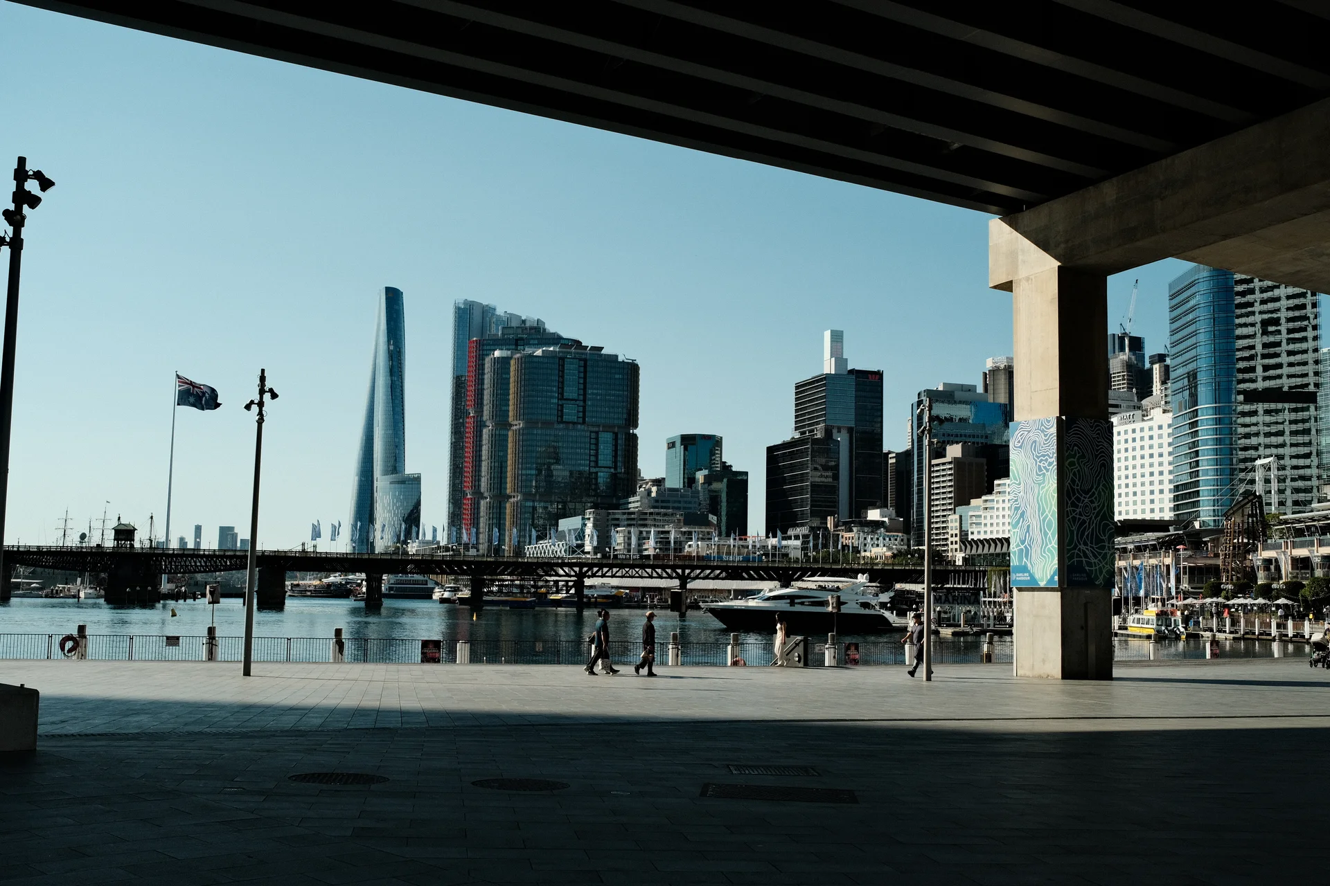 Sydney's waterfront skyline framed by the deep shadow of a concrete overpass.