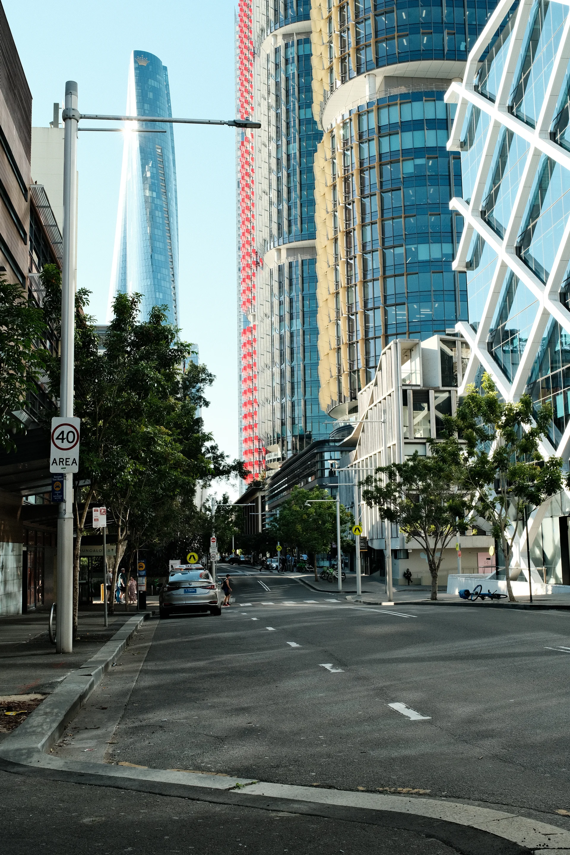A quiet city street framed by curved glass towers and white structural beams.